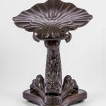 Sgabello da pianoforte in mogano scolpito. Seduta a forma di conchiglia sorretta da un delfino scolpito. Inghilterra, epoca Regency, inizi ‘800.